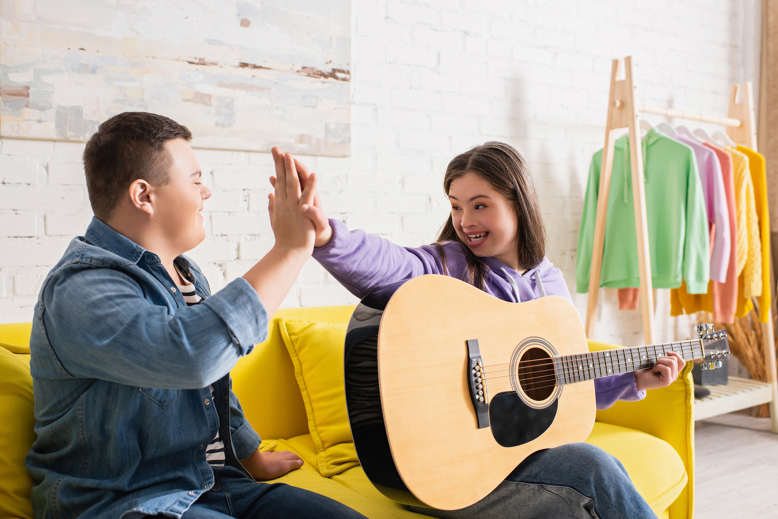 Positive teenagers with down syndrome giving high five near acoustic guitar at home