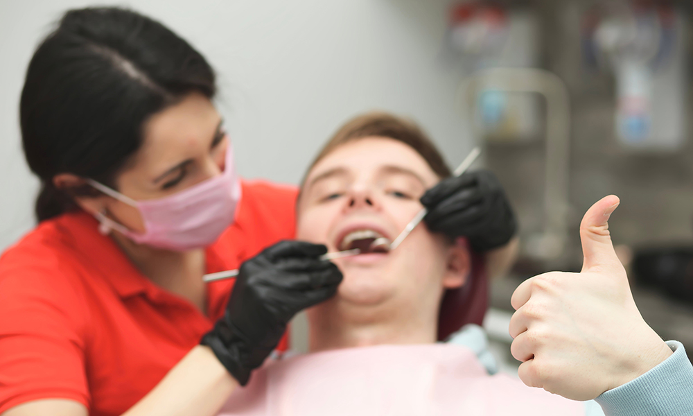 Happy satisfied guy shows thumb up sitting in dentist chair with woman dentist