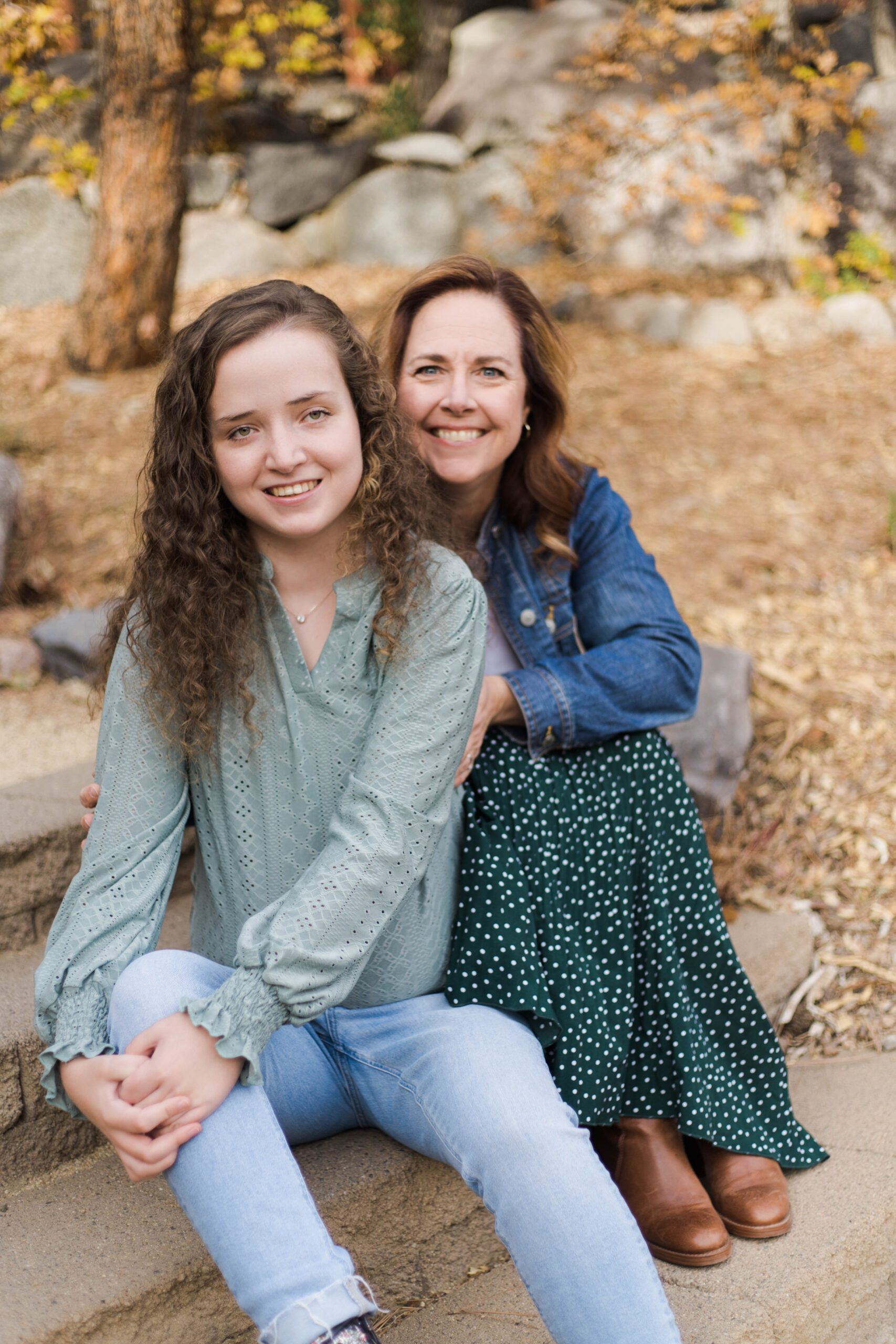 Diane sits with her arm around her daughter, outdoors, smiling